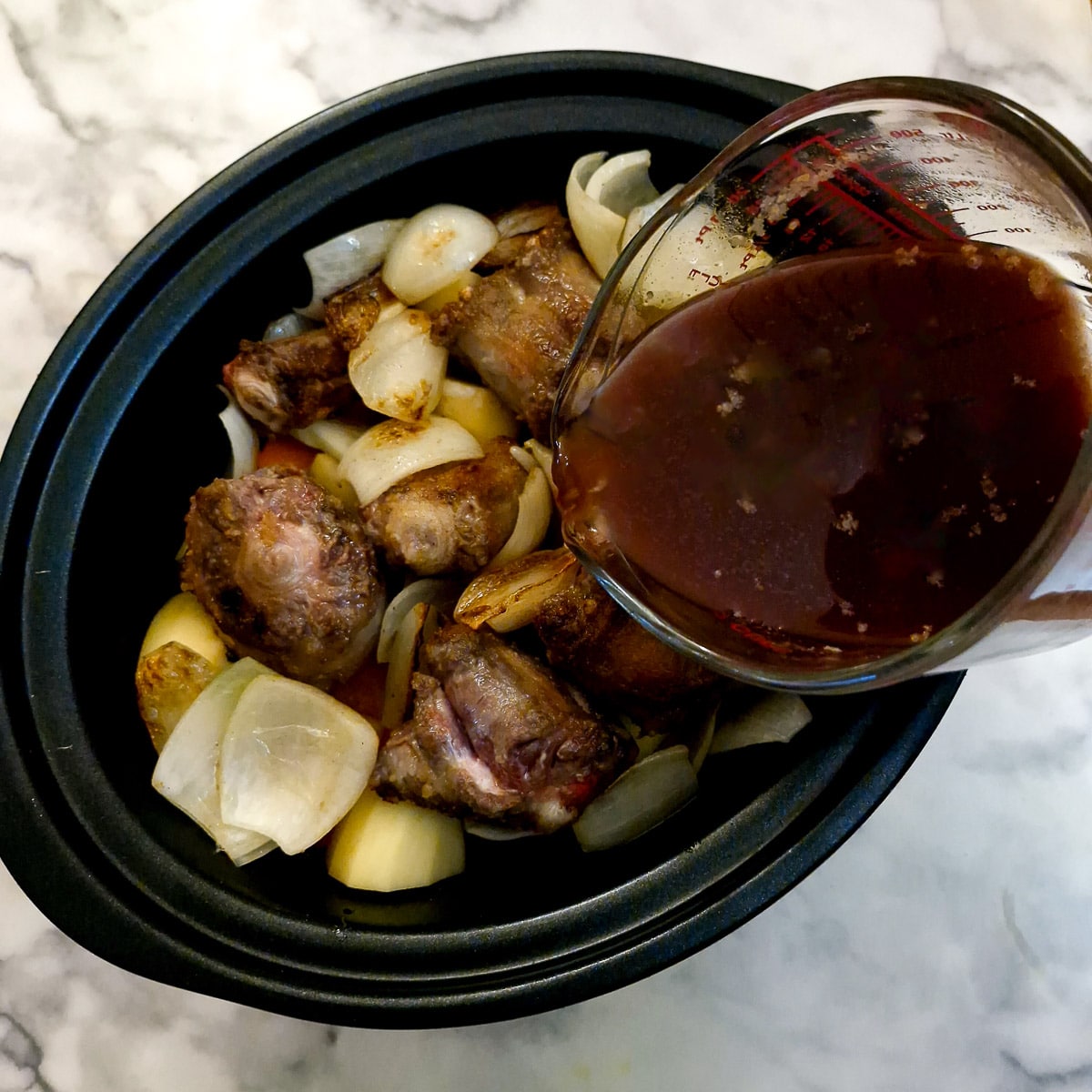 A jug of gravy being poured into the slow cooker.