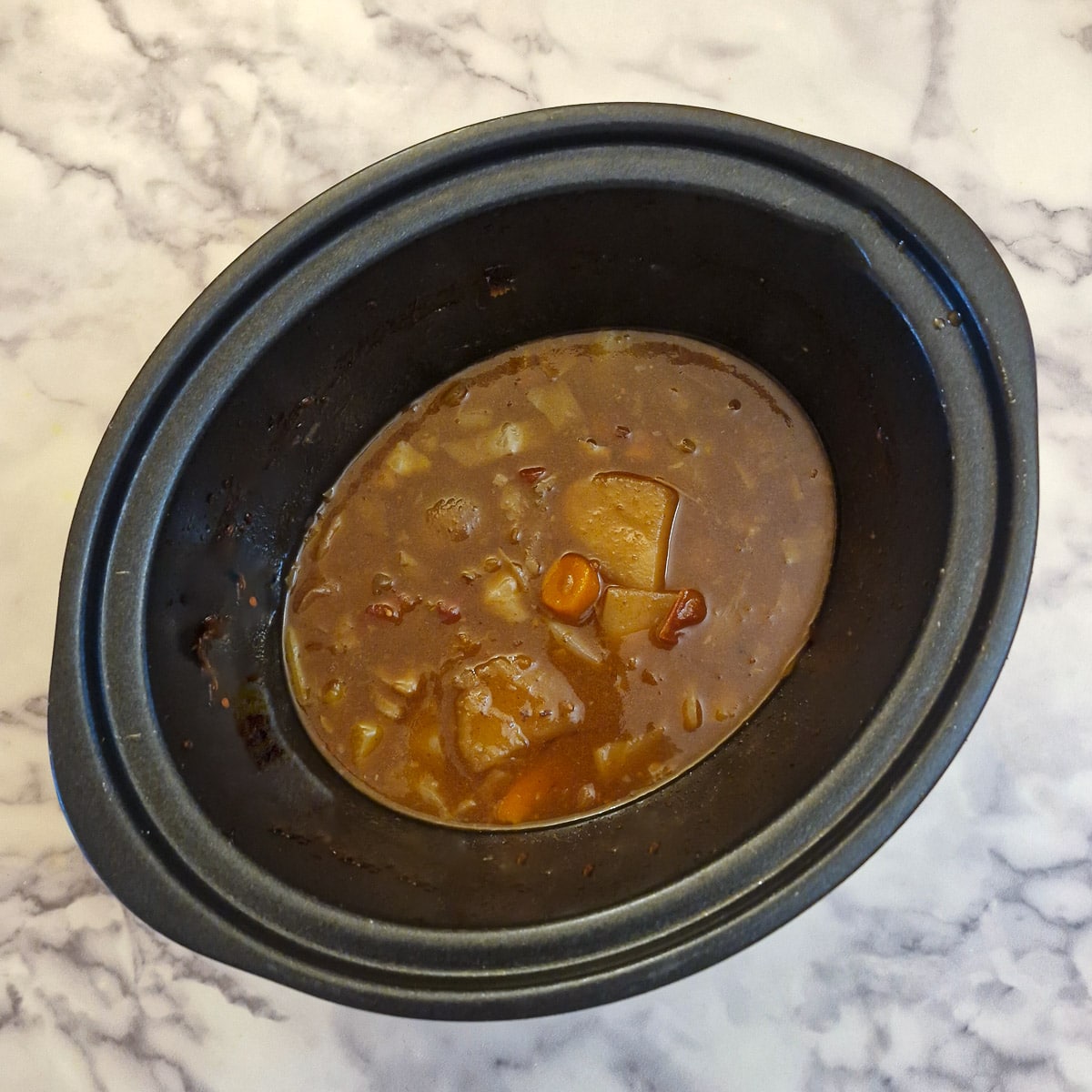 Cooking liquid and vegetables in the bottom of a slow cooker.
