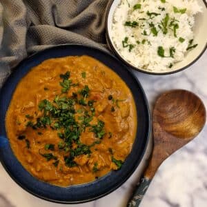 A black serving dish filled with chicken tikka masala with a dish of white rice in the background.