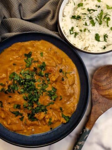 A black serving dish filled with chicken tikka masala with a dish of white rice in the background.