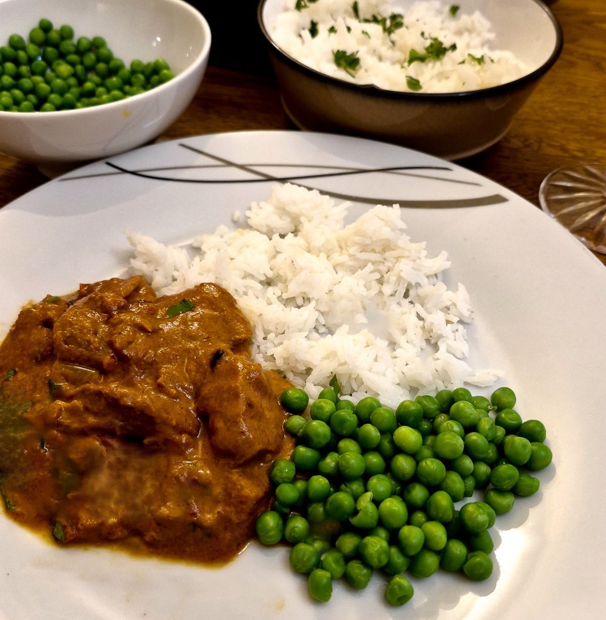 A plate of chicken tikka masala with rice and a side helping of peas.