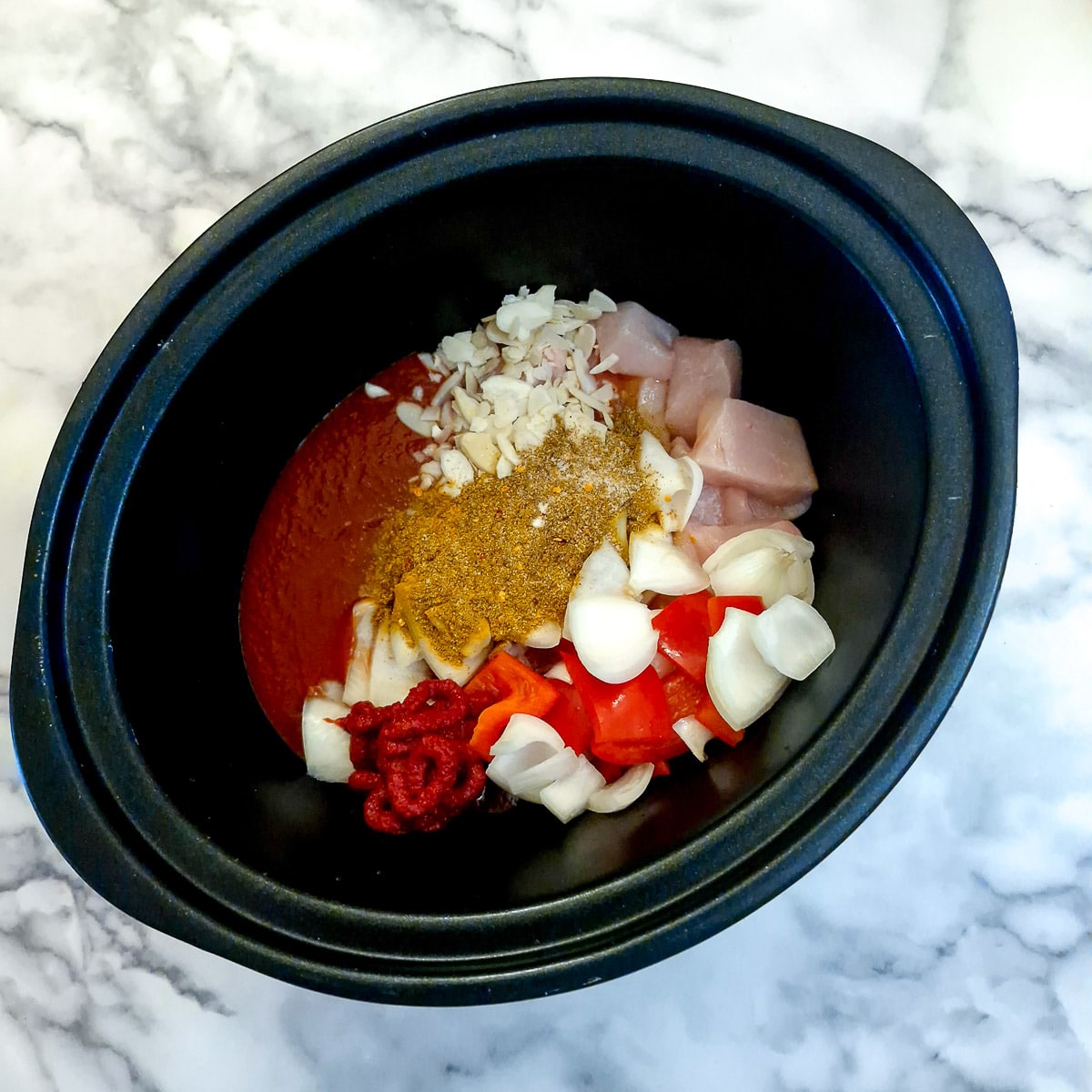 Raw chicken piecces, tomato passata and spices in a slow cooker.