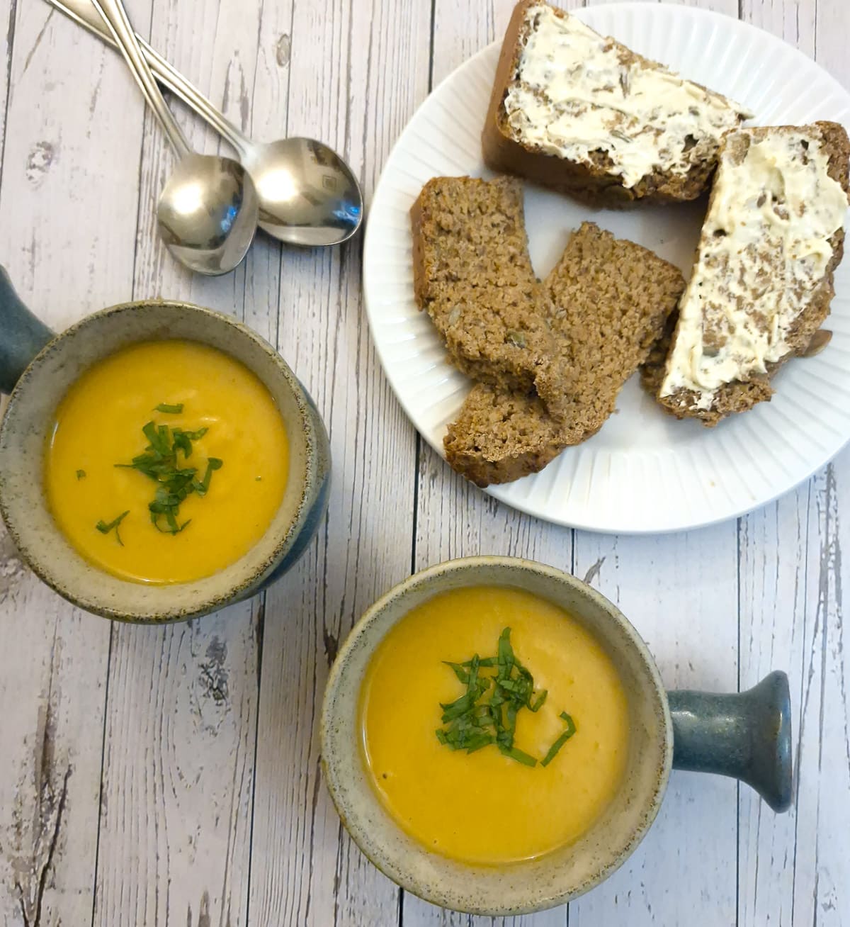 Two bowls of butternut soup on a table with a plate of sliced bread.