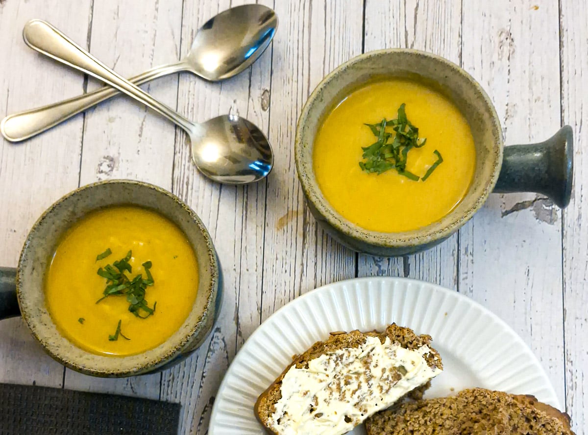 Two bowls of butternut soup on a table with spoons.