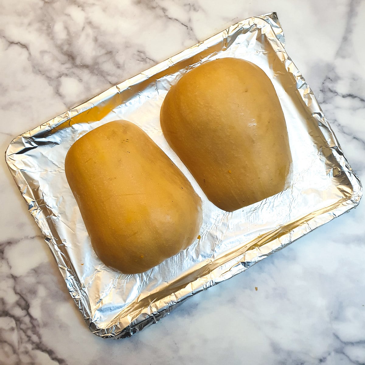 Two halves of butternut placed cut side down on a baking tray.