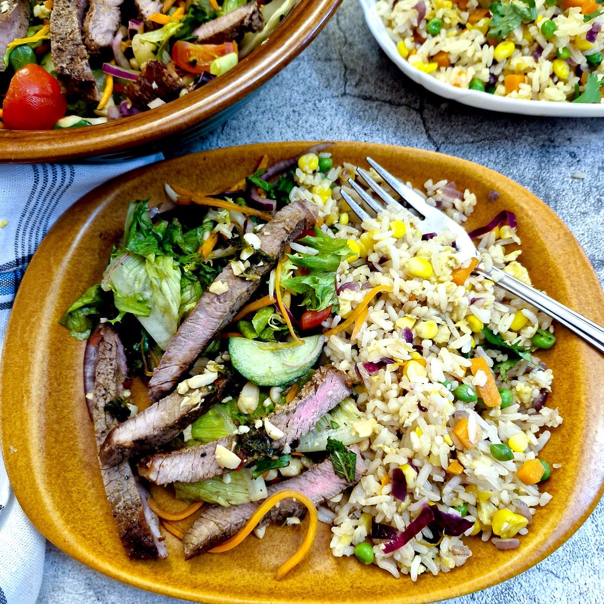 Thai beef salad on a brown plate with Thai vegetable rice.
