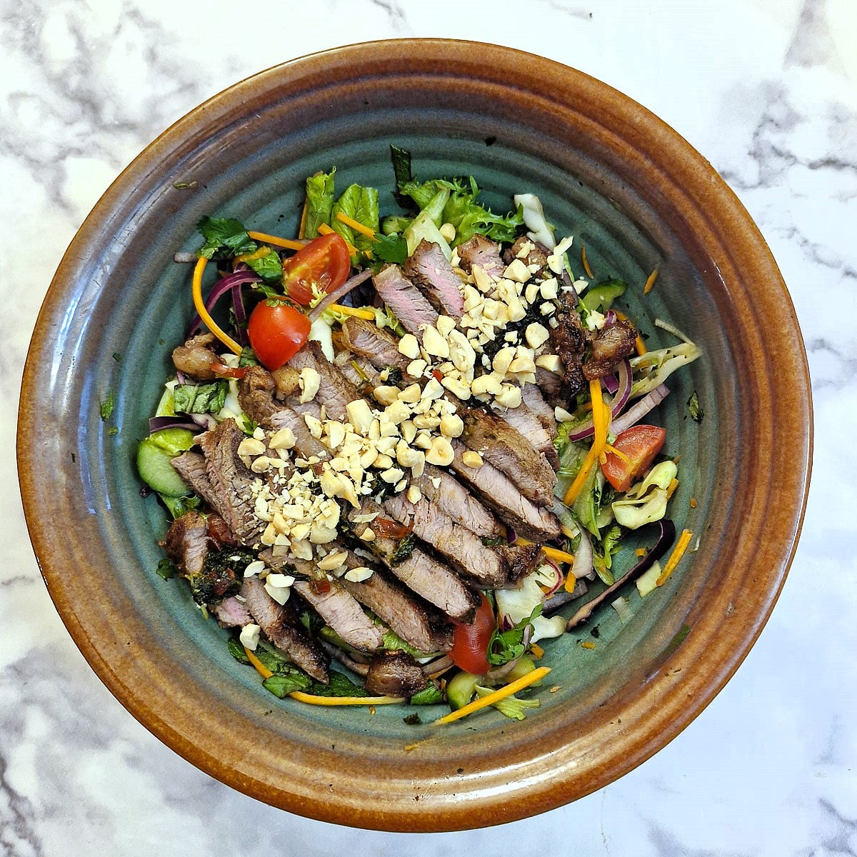 Overhead shot of a dish of Thai beef salad garnished with chopped peanuts.
