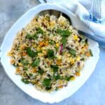 A white serving dish of Thai vegetable fried rice garnished with coriander.