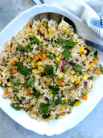 A white serving dish of Thai vegetable fried rice garnished with coriander.
