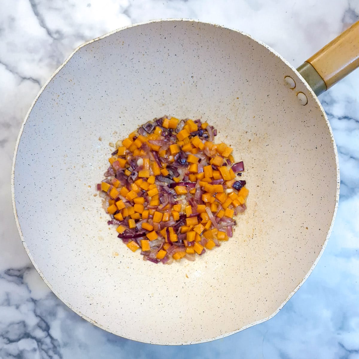 Chopped carrots and red onions frying in a wok.