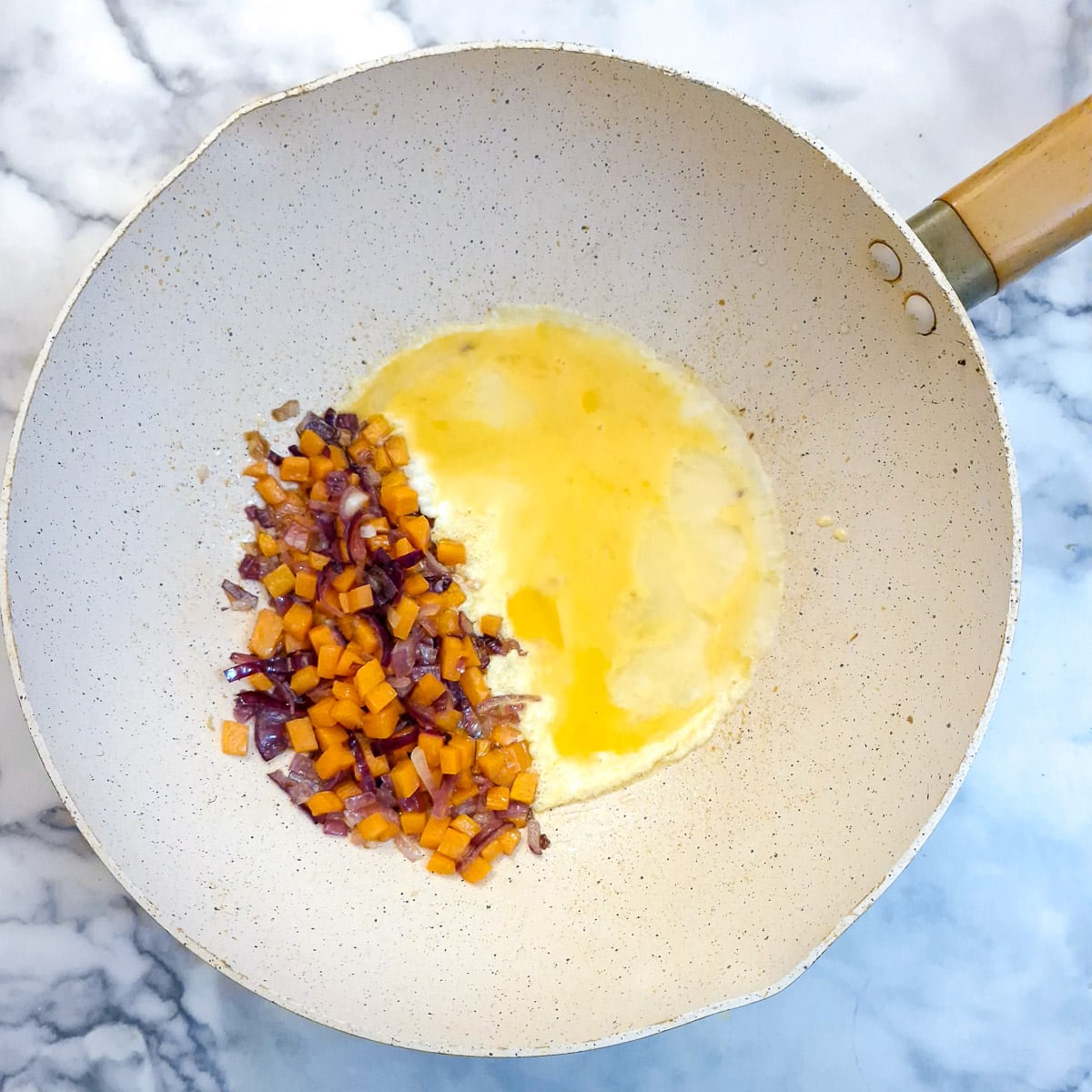 A beaten egg added at the side of carrots and onions in a wok.