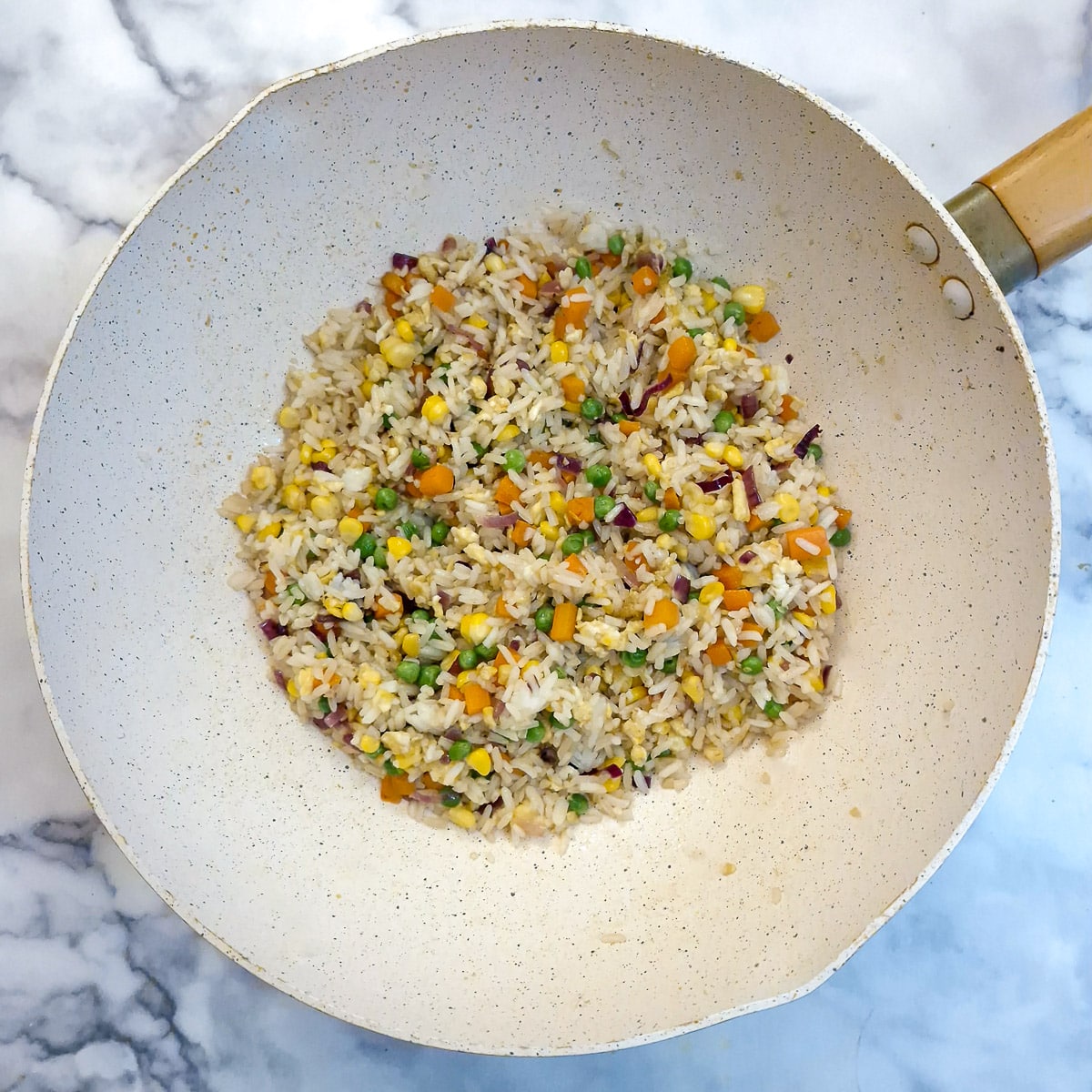 Thai fried rice mixed with sauce in a wok.