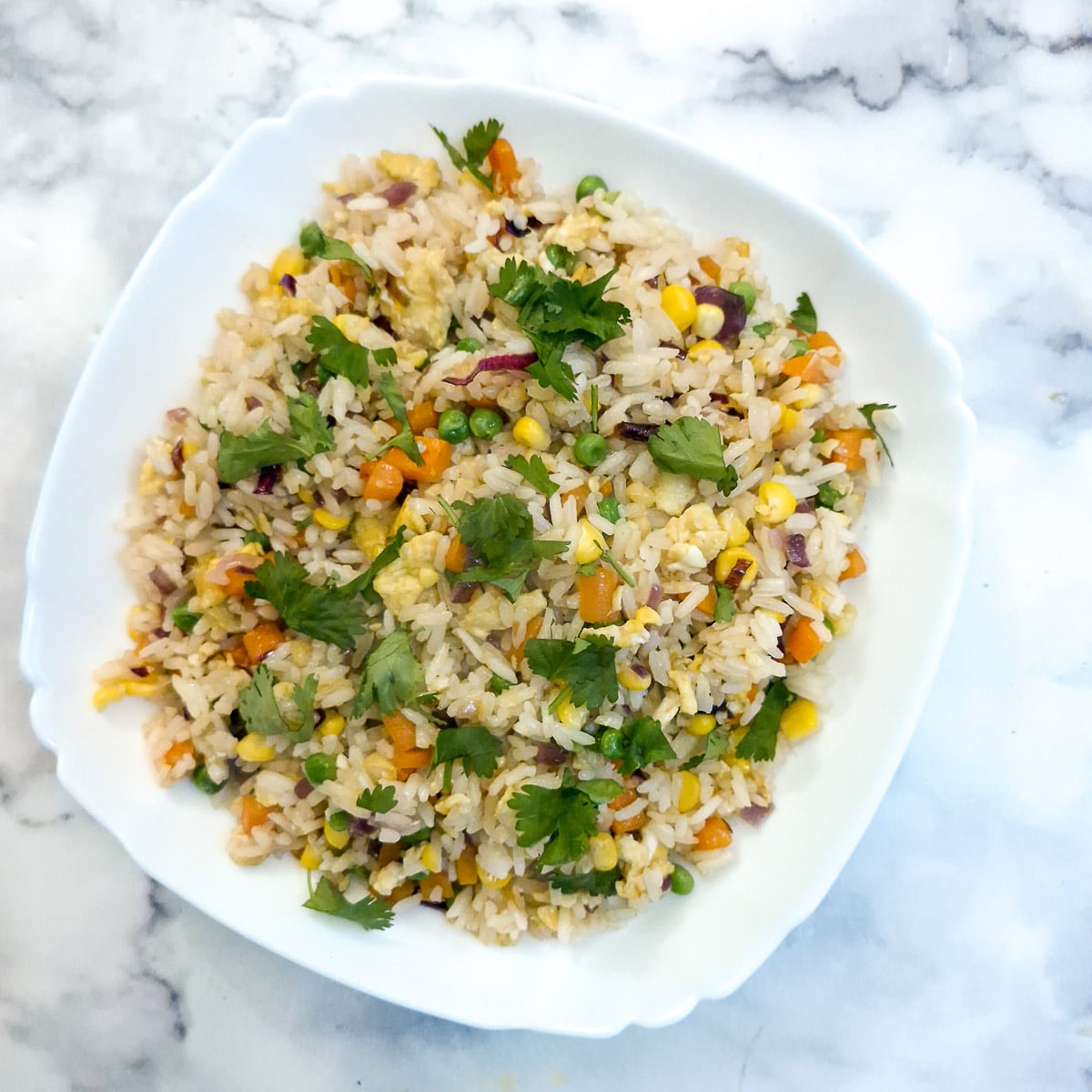 A white serving dish filled with Thai fried rice and garnished with chopped coriander.