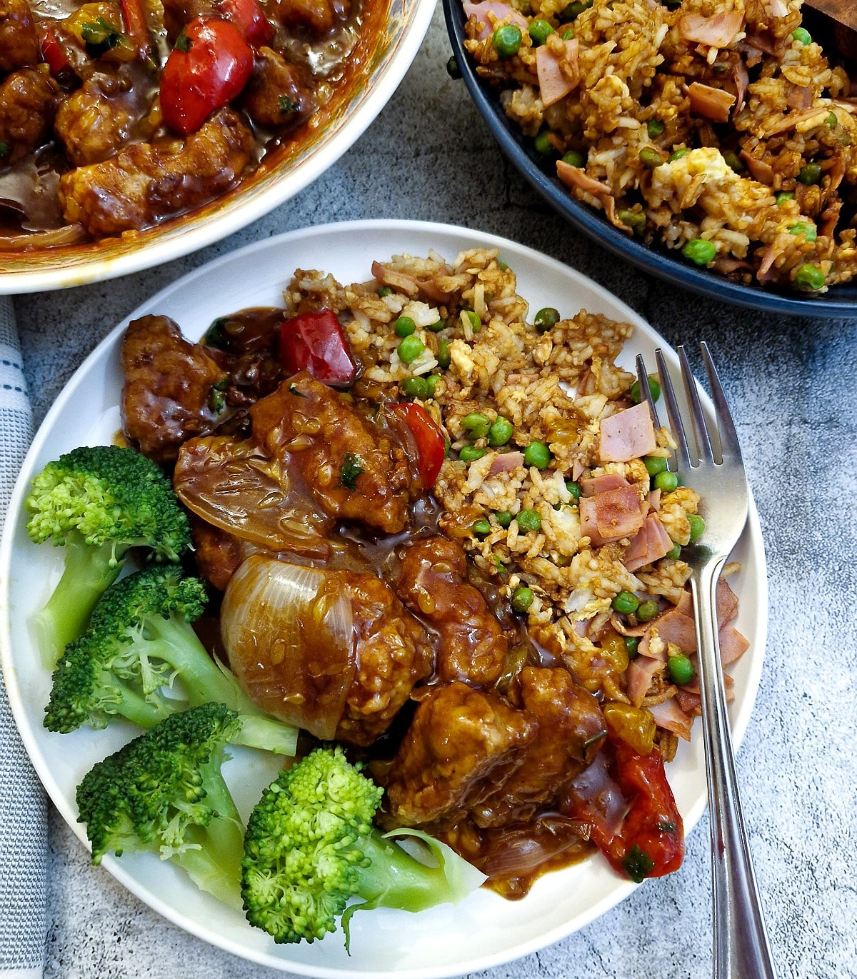 Crispy orange pork stir fry on a plate with egg fried rice and steamed broccoli.