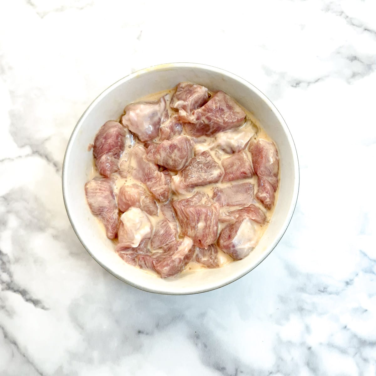 Cubes of pork marinating in beaten egg and cornflour.