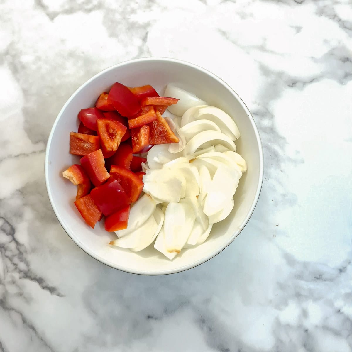 Slices of capsicum and onions in a white dish.