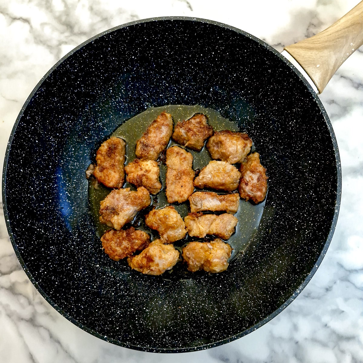 Pieces of pork frying in a wok.