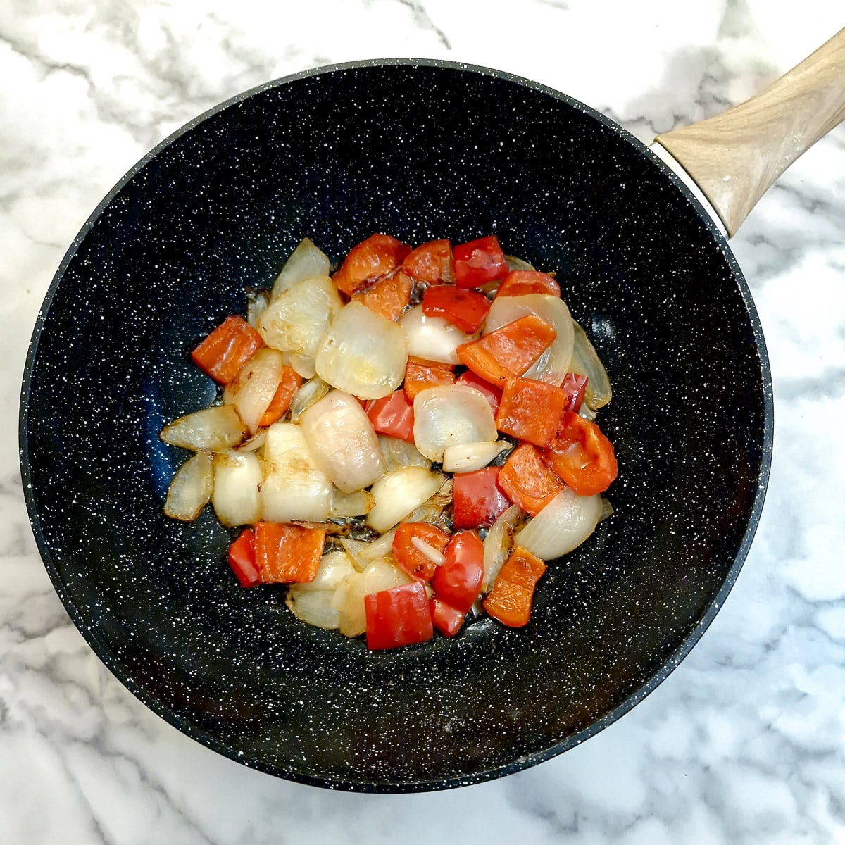 Onions and capsicum softening in a wok.