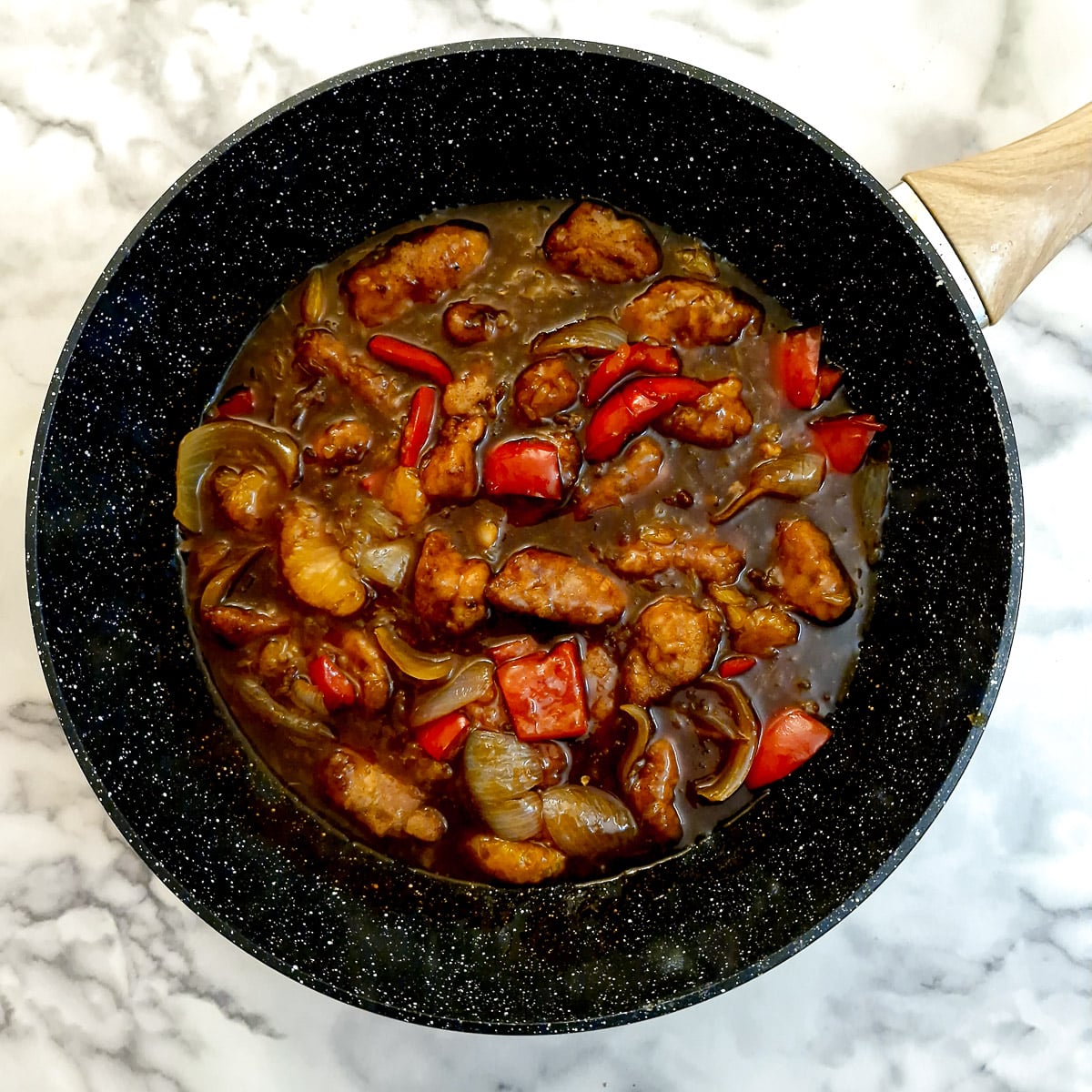 Cubes of fried pork added to the sauce in a wok.