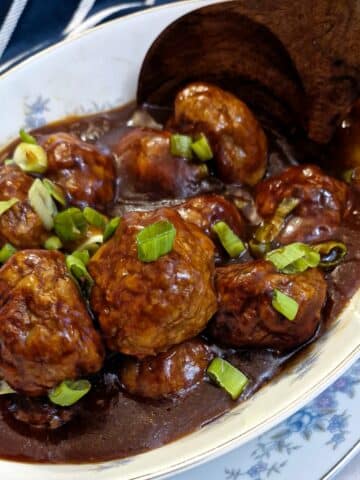 A dish of sticky chicken meatballs with a large wooden serving spoon,
