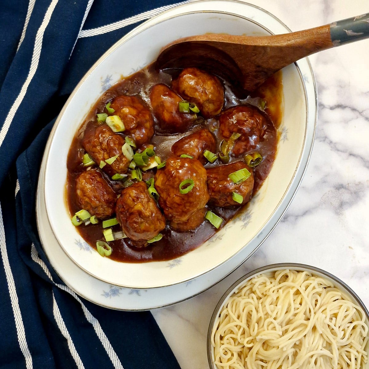 A dish of easy Asian chicken meatballs in sauce, next to a bowl of Chinese noodles.