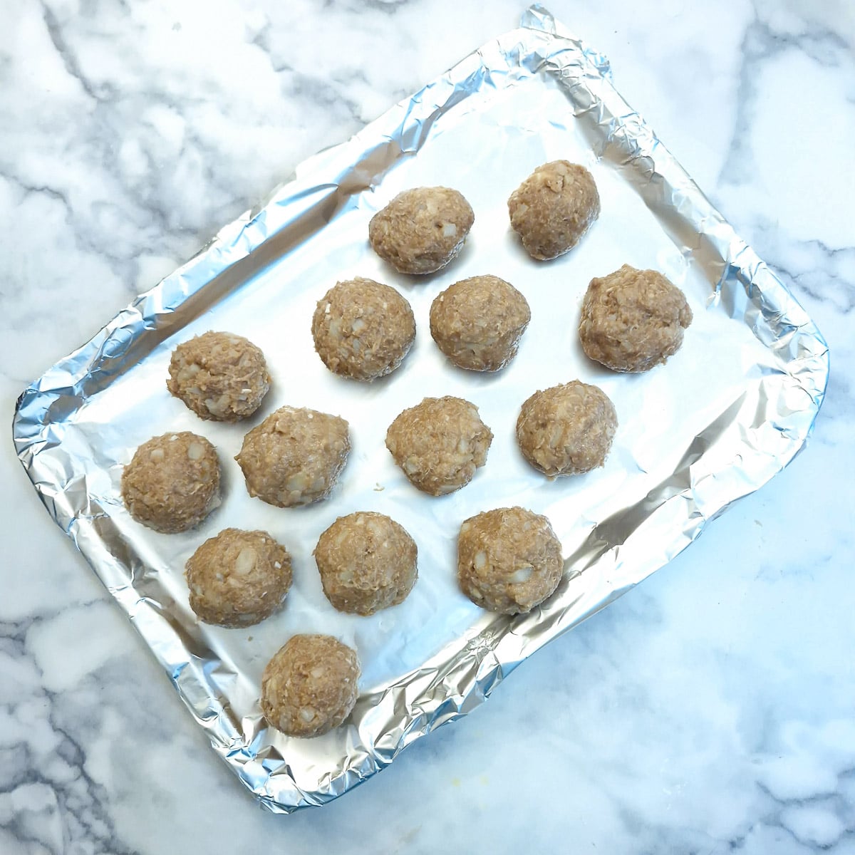 Uncooked meatballs arranged on a baking tray.