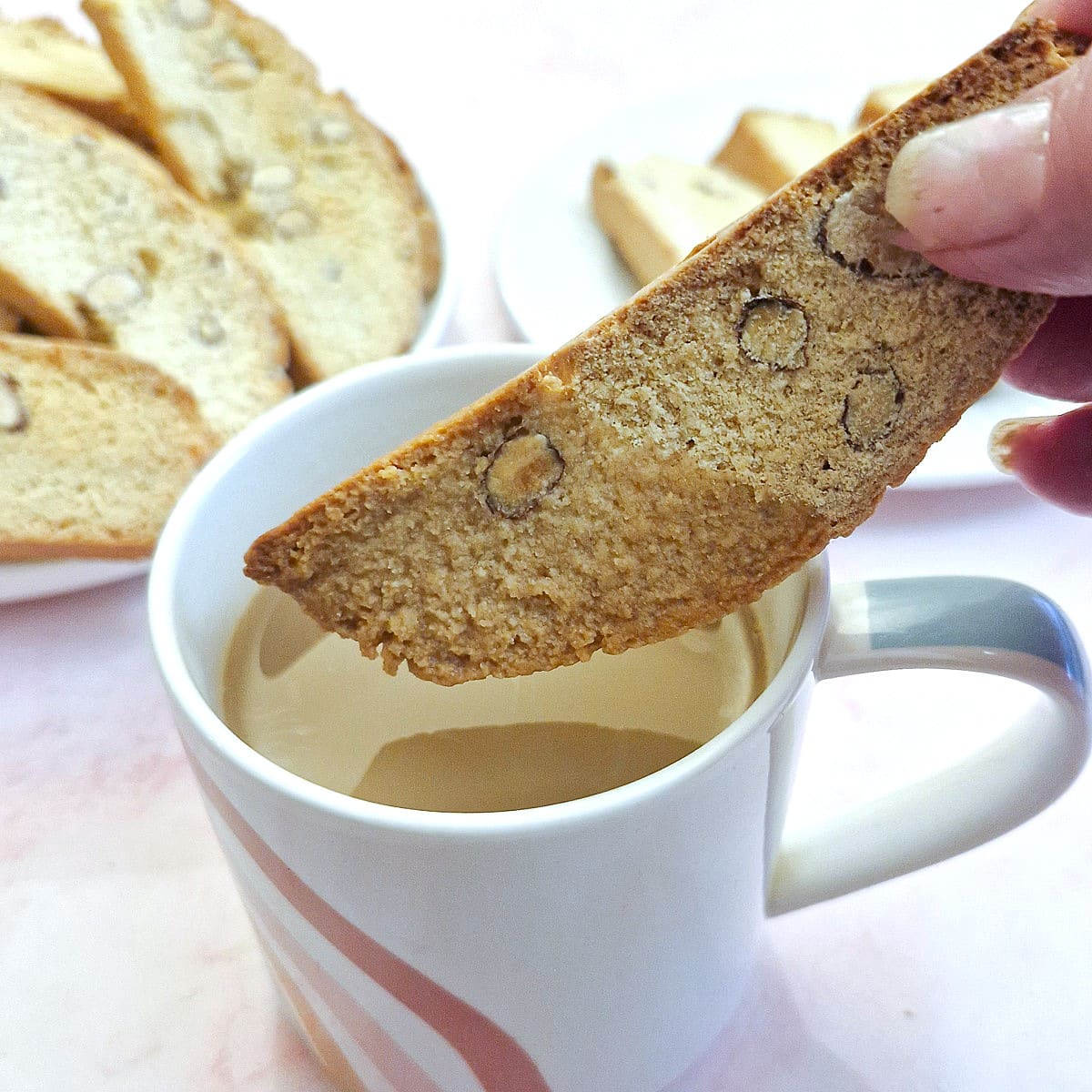 An almond biscotti being dunked in a mug of coffee.
