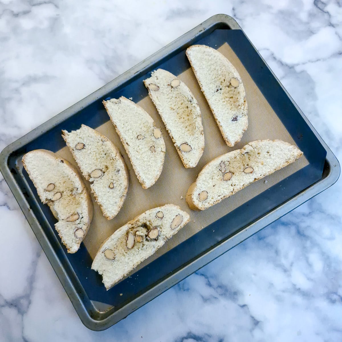 Baked biscotti cut into slices and arranged on a baking sheet to be baked for a second time.