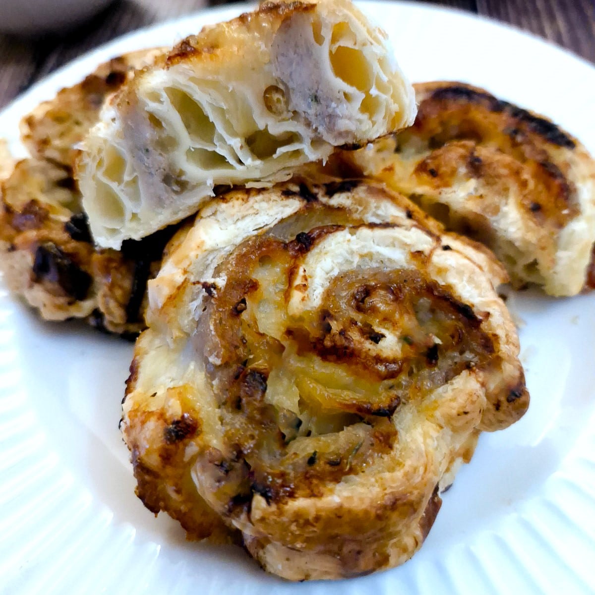 2 sausage and onion pinwheels on a white plate with a third one cut open to show the inside.