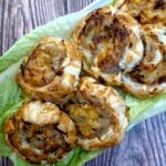 A pile of sausage and onion pinwheels on a bed of lettuce leaves.