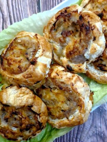 A pile of sausage and onion pinwheels on a bed of lettuce leaves.