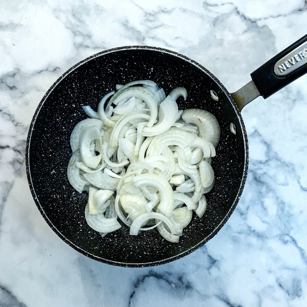 Raw sliced onions in a frying pan.