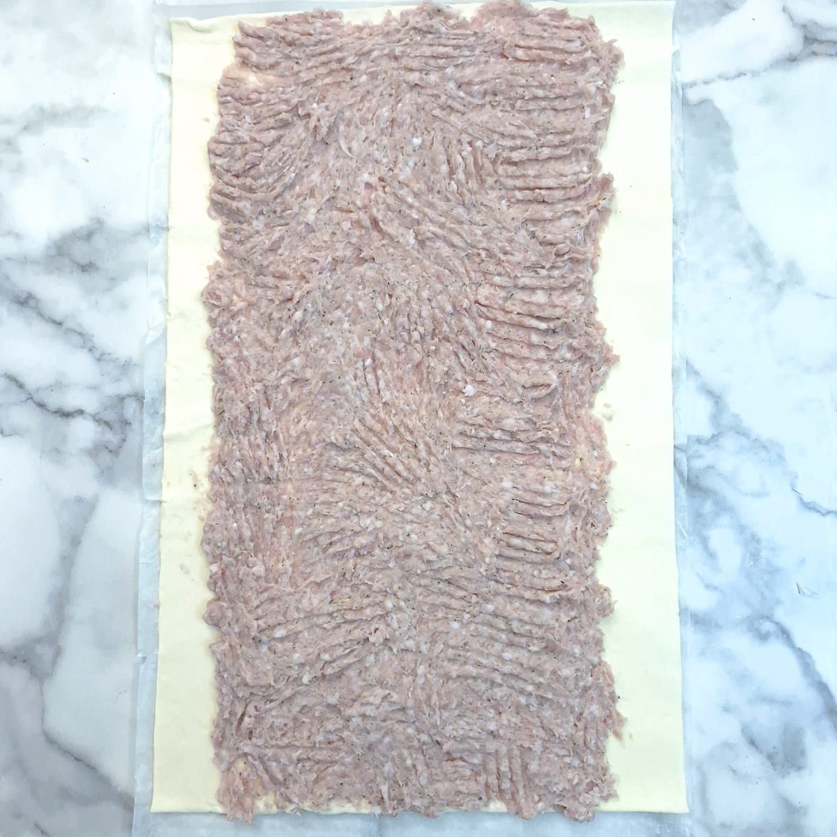 Sausage meat spread onto a sheet of puff pastry.
