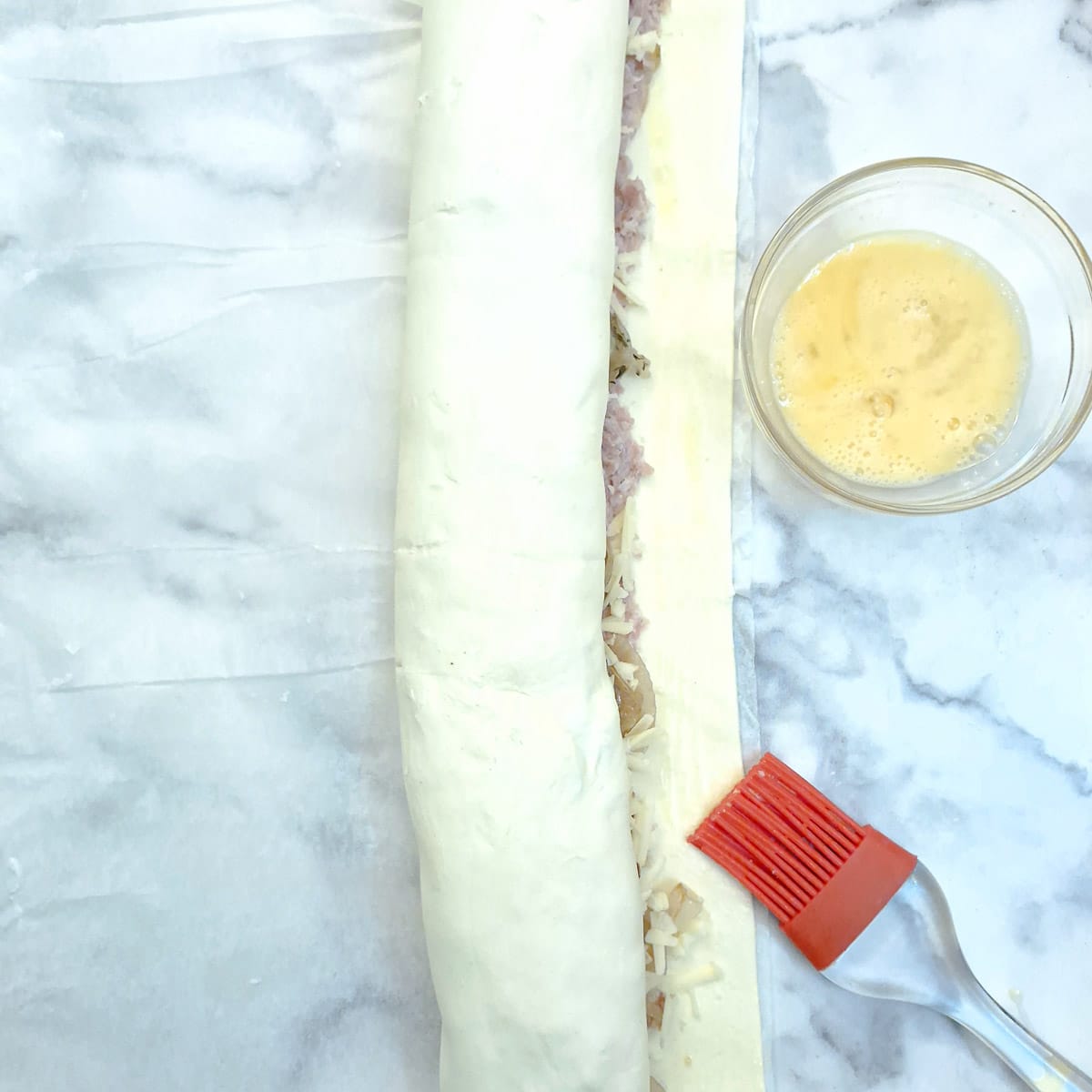 A rolled sausage roll being sealed with egg wash.