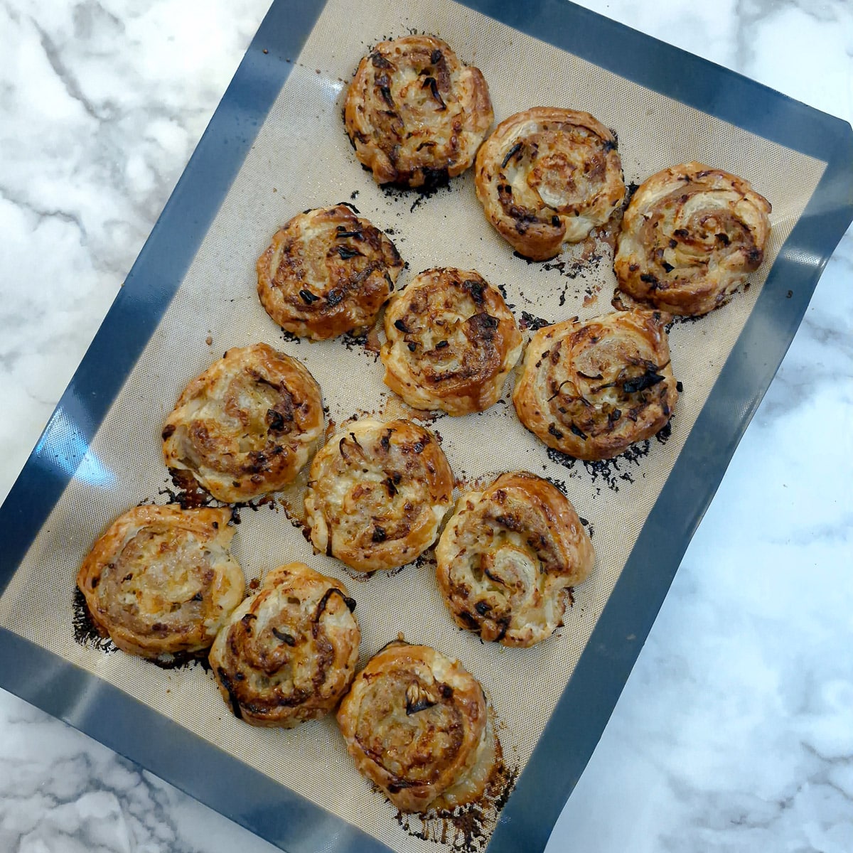 Baked sausage and onion pinwheels on a baking tray.