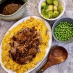 A serving platter piled with root vegetable mash and filled with slow cooker brisket and onion gravy.