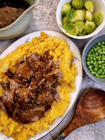 A serving platter piled with root vegetable mash and filled with slow cooker brisket and onion gravy.