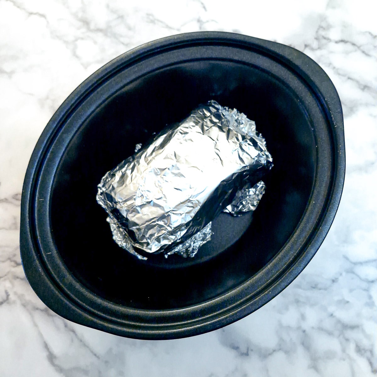 A tin foil-wrapped piece of brisket in a slow cooker.