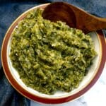 A red-rimmed serving dish of spring green potato mash with a wooden serving spoon.