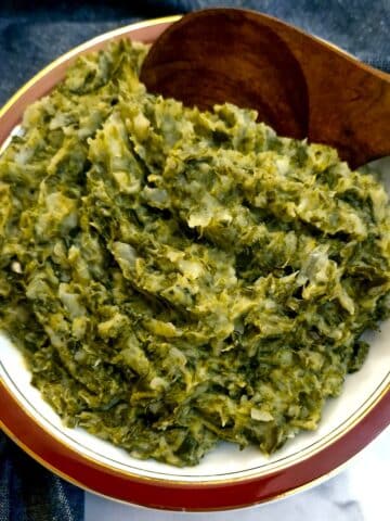 A red-rimmed serving dish of spring green potato mash with a wooden serving spoon.