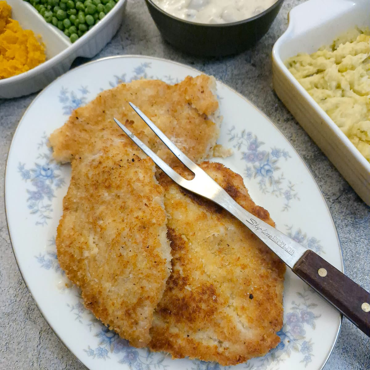 Crumbed chicken schnitzels on a serving plate surrounded by dishes of vegetables.