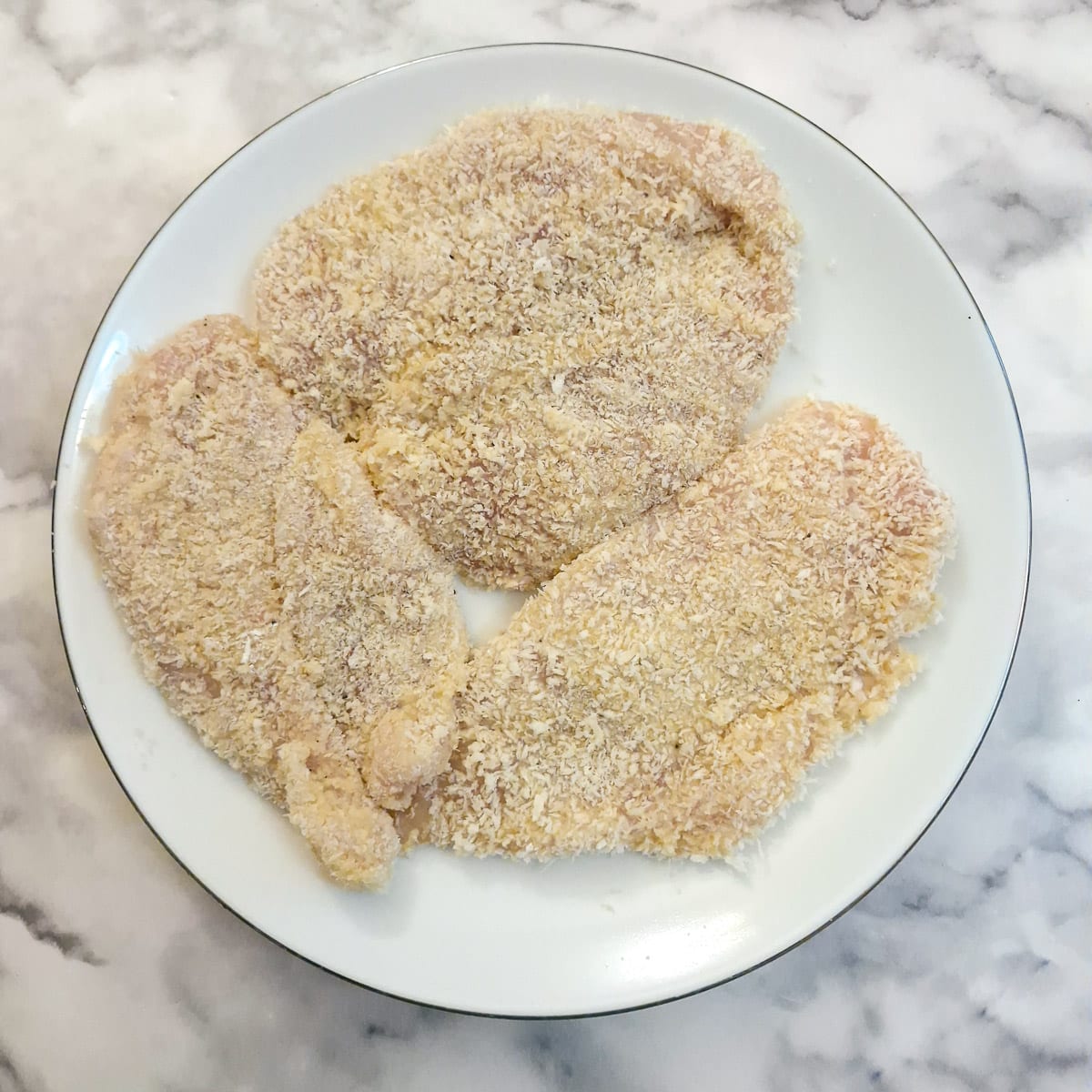 3 uncooked crumbed chicken schnitzels on a plate.