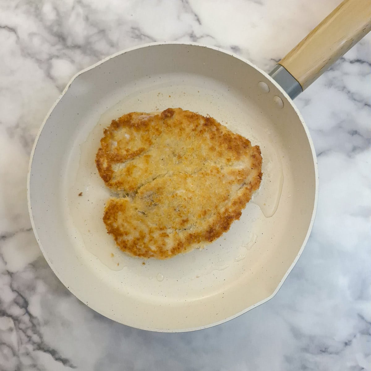 A chicken schnitzel browning in a frying pan.