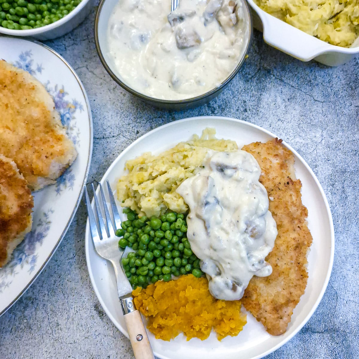 A crumbed chicken schnitzel on a white plate with vegetables and mushroom sauce.