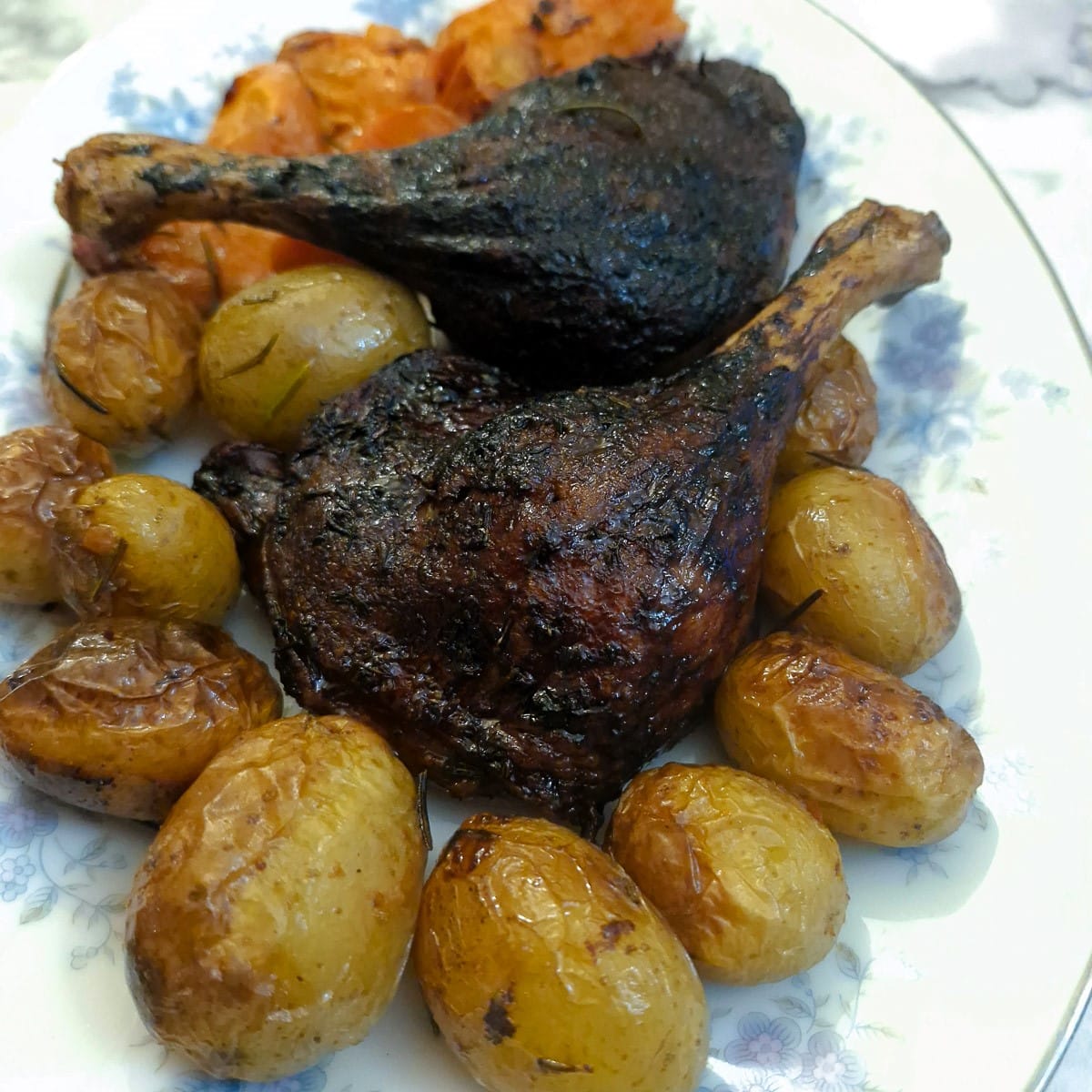 Two red-wine braised duck legs on a bed of roast potatoes an carrots.