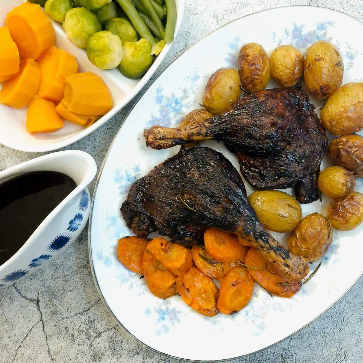 Two roasted duck legs on a serving platter with potatoes and carrots.