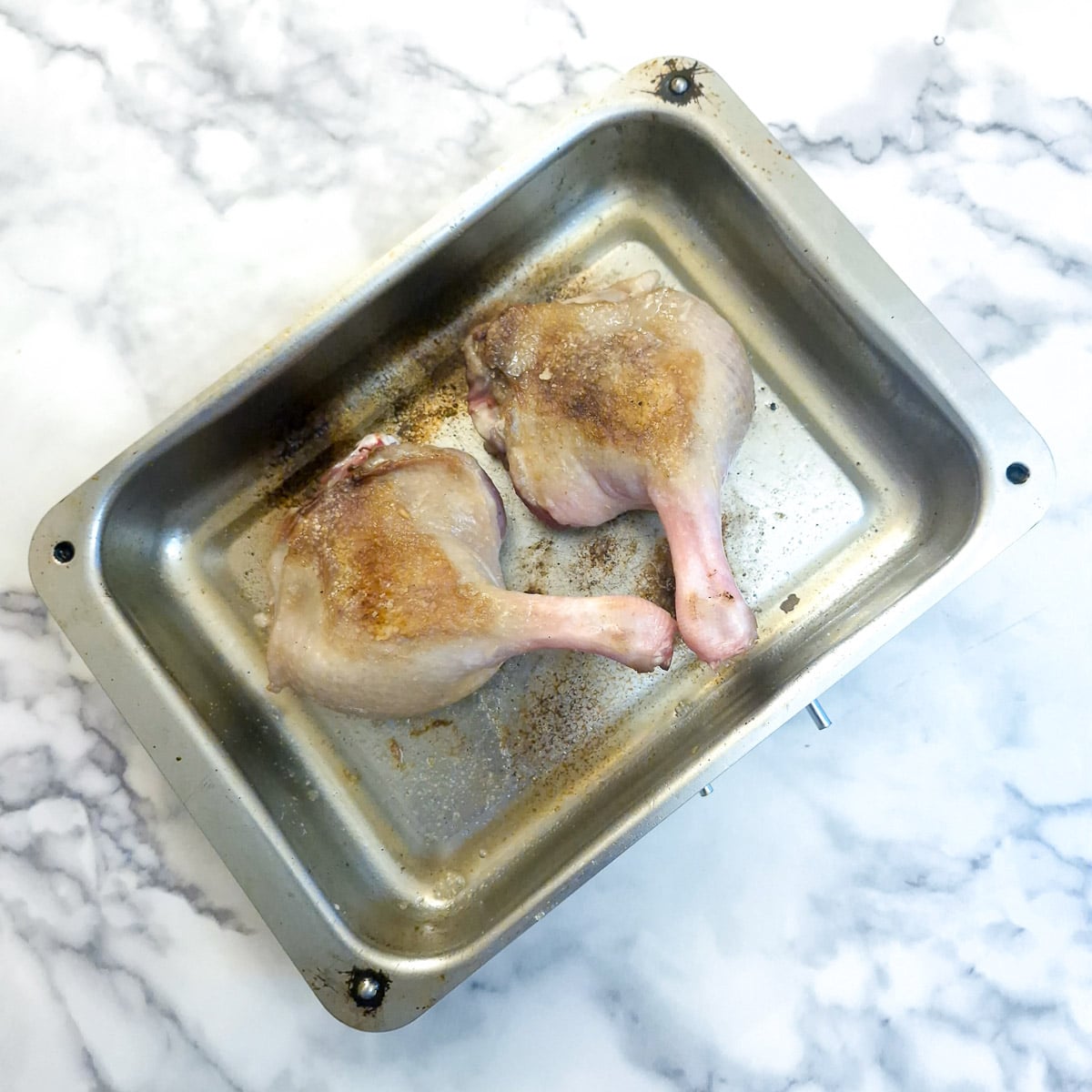 Two browned duck legs in a roasting tray.