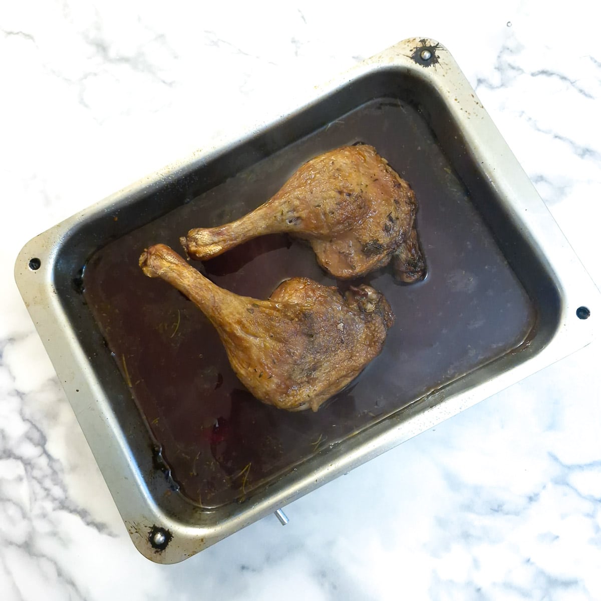 2 duck legs in a roasting pan covered in red wine sauce.