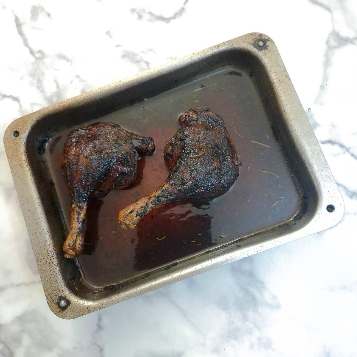 Two braised duck legs in aroasting pan of red wine sauce.
