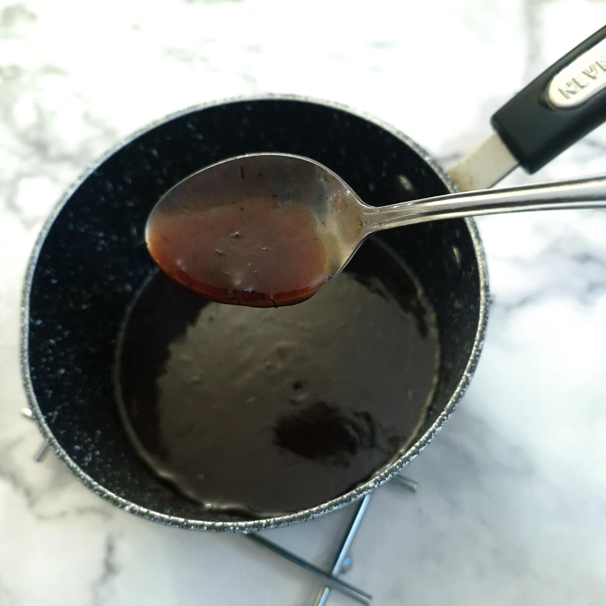 Thickened red wine sauce in a saucepan with a spoon showing the consistency.